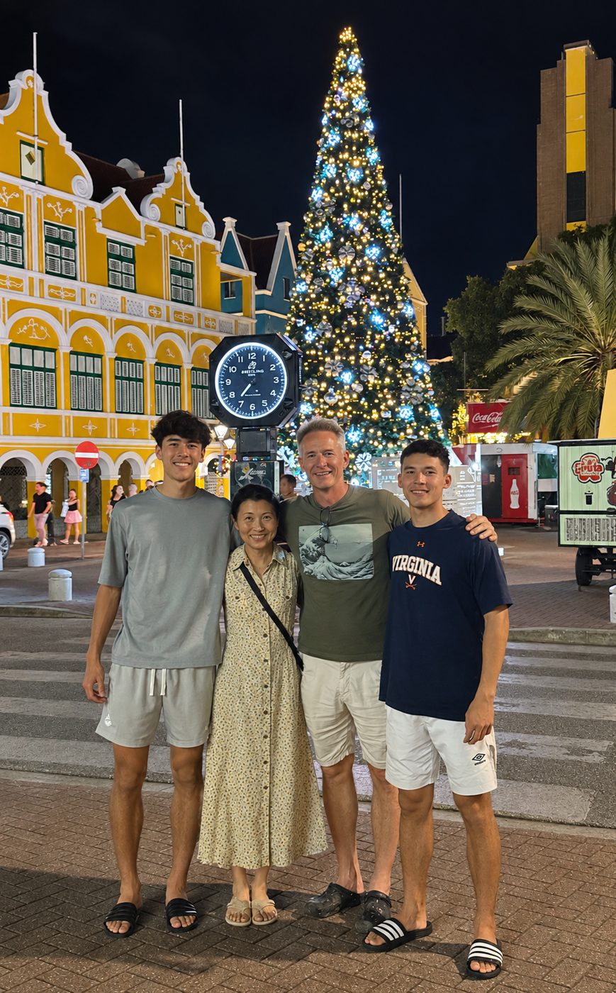 Chris Ognek with his wife and two sons at night in front of a lit Christmas tree and colorful Dutch-colonial buildings